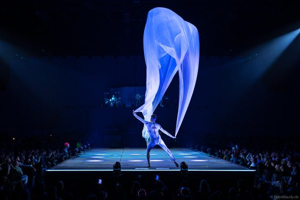 Turner performen mit einem Tuch im Luftstrom eindrucksvoll im Licht auf der Bühne bei DJ BoBo – The Great Adventure